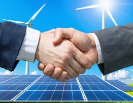 Business professional and government official shaking hands with wind turbines and solar panels in the background, representing a partnership in renewable energy financing.