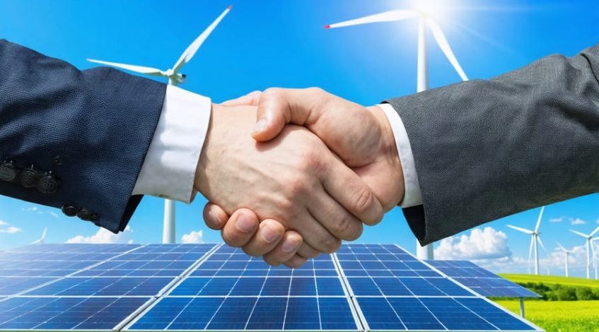 Business professional and government official shaking hands with wind turbines and solar panels in the background, representing a partnership in renewable energy financing.