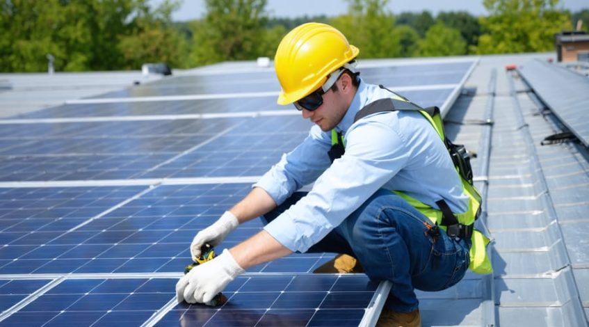 A solar technician on a rooftop, showcasing proper use of electrical safety gear and adherence to safety protocols during solar panel installation.
