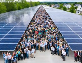 Diverse community members gathered around a large-scale solar installation, symbolizing collaboration and sustainable development with residential homes and local businesses in the background.