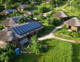 "Aerial view of an off-grid community with solar panels and wind turbines, highlighting the integration of renewable energy systems within a green, self-sufficient environment."