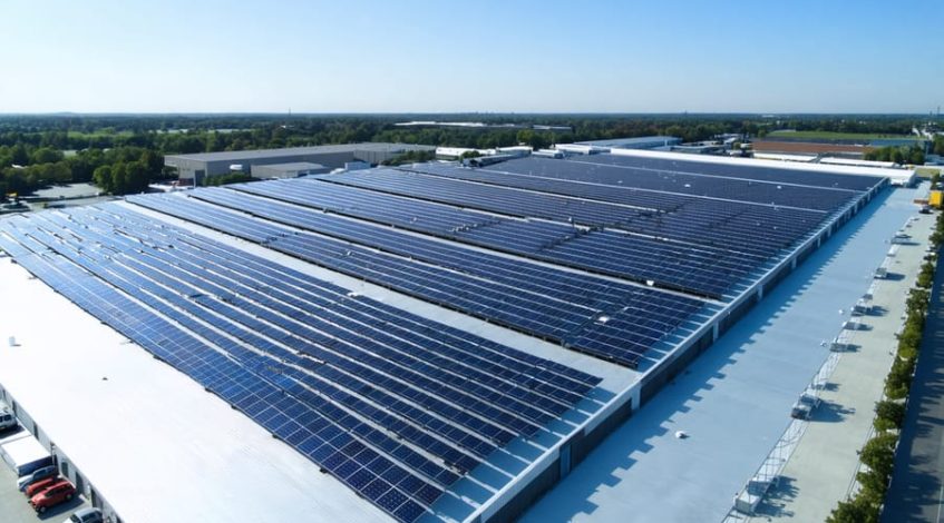 "Aerial view of a modern warehouse rooftop covered with extensive solar panel arrays, surrounded by industrial buildings, showcasing the integration of solar energy in warehouse operations."