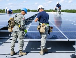 Veterans and solar installation team collaborating to install solar panels on a commercial rooftop, showcasing partnership and sustainability.