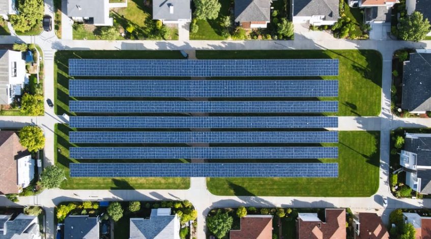 Aerial view of a community solar installation powering multiple homes in a suburban neighborhood, with residents enjoying outdoor activities nearby.