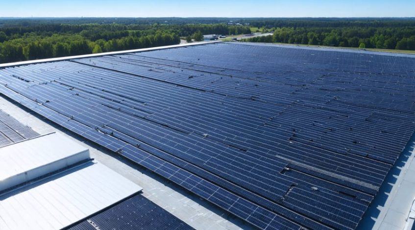 Aerial view of a manufacturing facility rooftop covered with solar panels under a clear blue sky, symbolizing industrial solar power integration and efficiency.