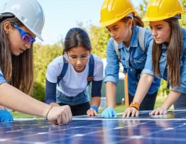 A diverse group of K-12 students enthusiastically working with solar panels and equipment outdoors, alongside educators and solar industry professionals, illustrating hands-on learning and workforce development in renewable energy.