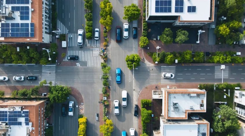 A dynamic aerial view of a business district with solar-paneled rooftops, electric vehicle charging stations, and a variety of electric commercial vehicles, symbolizing the shift to a zero-carbon future.