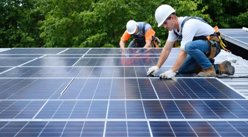"Team of workers installing solar panels on a rooftop, surrounded by greenery, representing career opportunities in renewable energy."