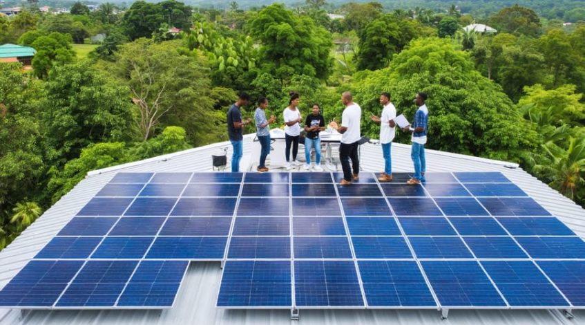 "Community members of diverse backgrounds engaged in a planning meeting with financial advisors and technical experts, discussing the implementation of solar microgrids surrounded by rooftops covered with solar panels and lush greenery, symbolizing the fusion of sustainable energy and community-driven finance."