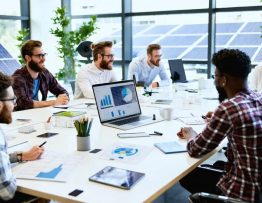 Entrepreneurs in a solar energy incubator workspace collaborating on innovative solar technology projects, with solar panel models and technical drawings visible.